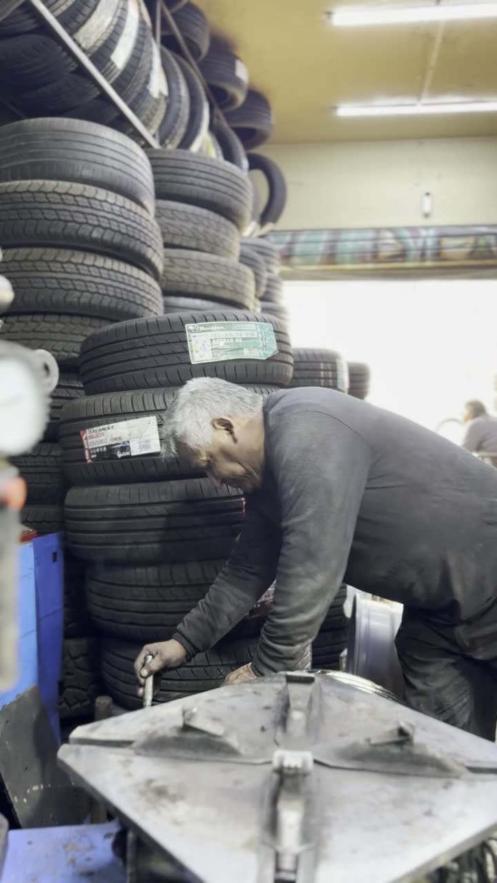 Maestro haciendo el apriete final de la rueda junto al stock de neumáticos